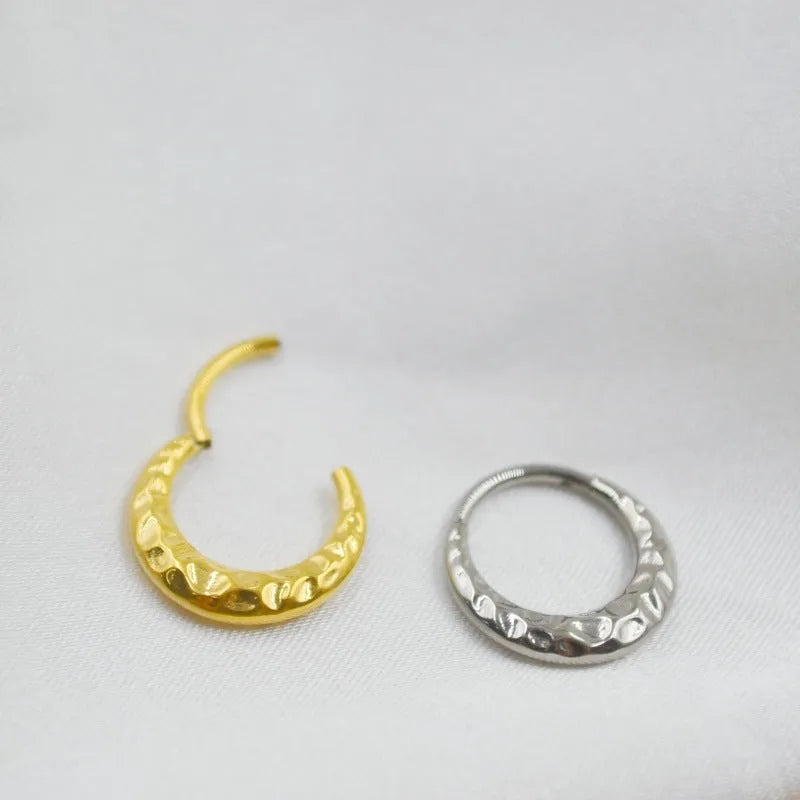 Close-up of a concave-convex carved titanium nose ring in gold finish on a grey background.