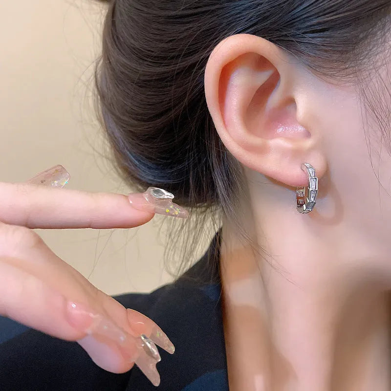 Silver-toned copper eardrop earring with geometric shape and needle post on white background