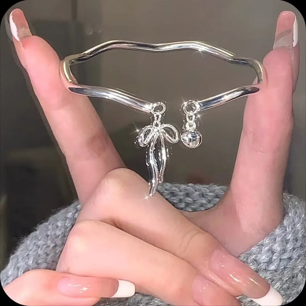 Silver adjustable bracelet with a bow charm and an opening bell charm on a model's wrist.