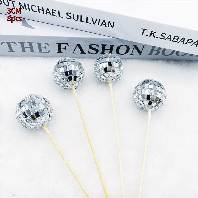 Glass disco ball cake decoration with wooden stick on a cake, showing reflective surface.