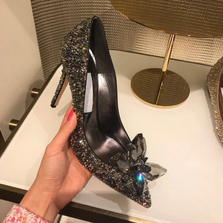 Gold women's high heels with pointed toe, rhinestone details, bow and stiletto heel on a plain background.