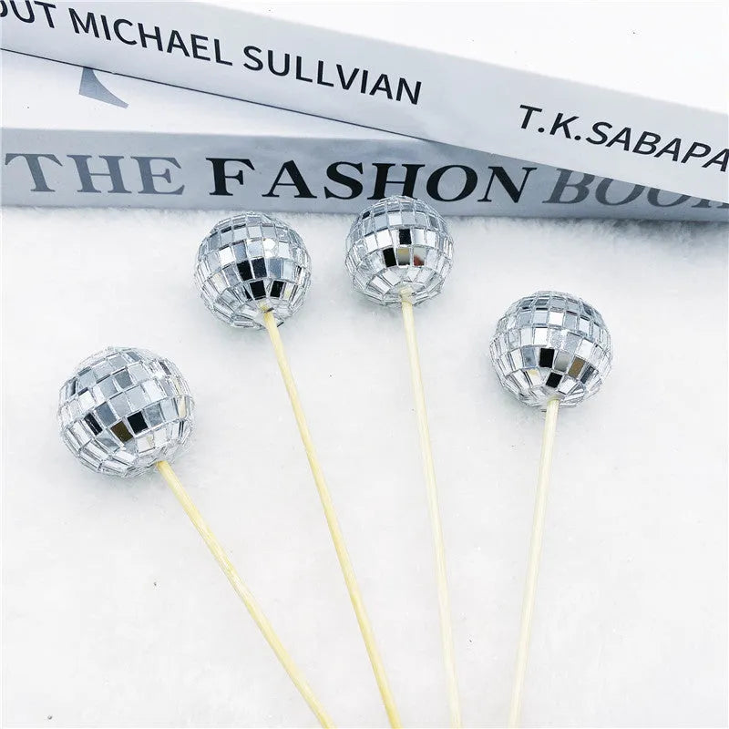 Glass disco ball cake decoration with wooden stick on a cake, showing reflective surface.