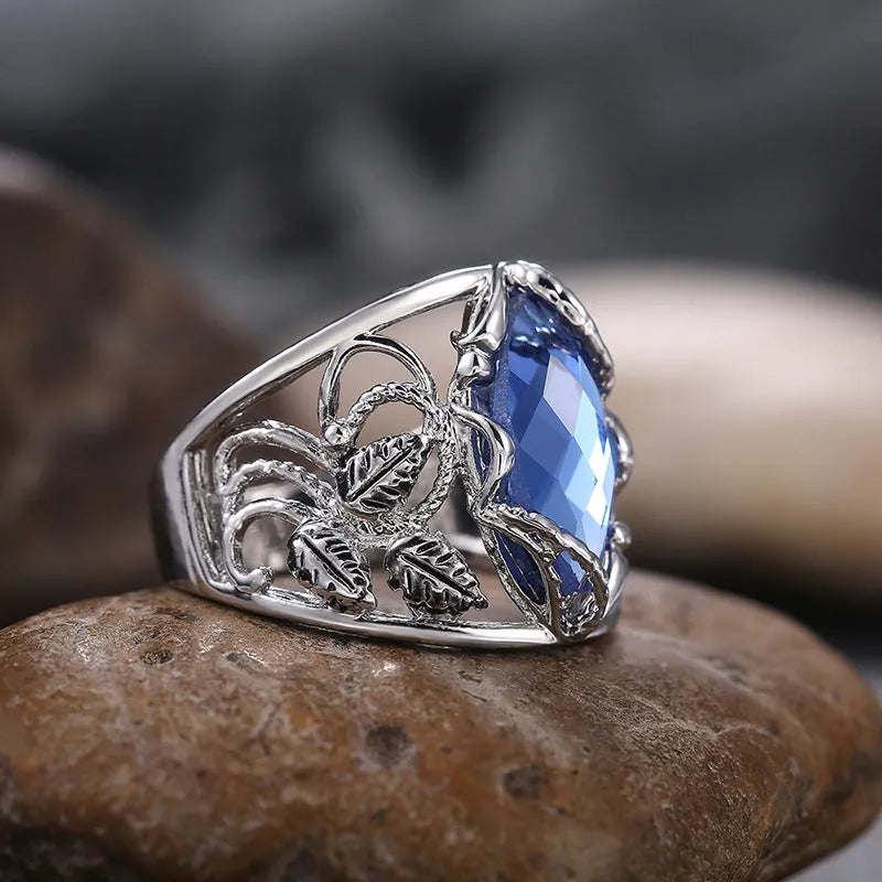 Close-up of a blue crystal horse eye-shaped geometric alloy ring on a person's finger.