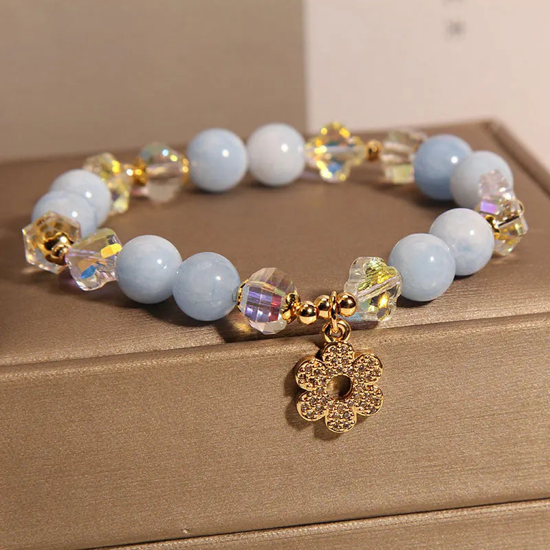 Women's aquamarine crystal bracelet with a four-leaf clover charm and a pearl accent on a model's wrist.