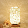 Handmade brown hemp rope spherical desk lamp with a solid wood base on a desk.