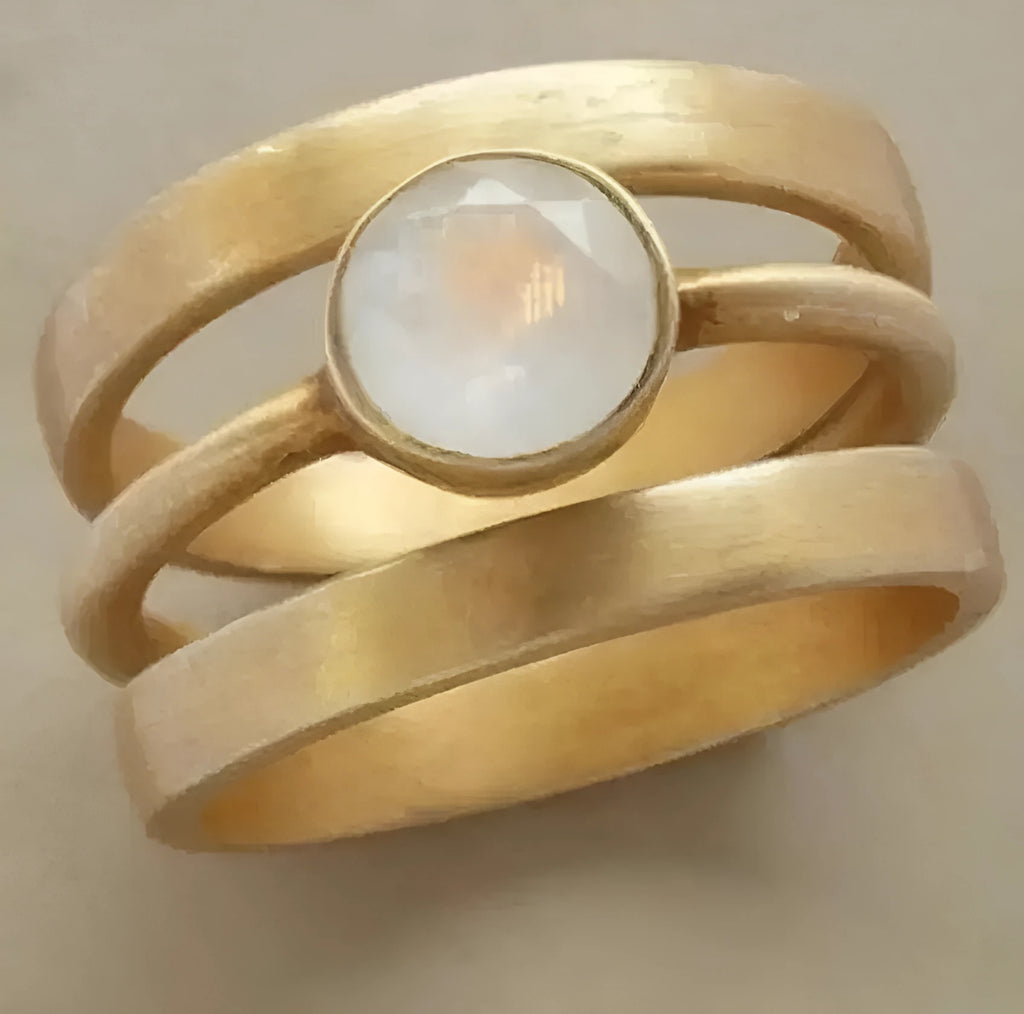 Gold geometric hollow ring with a small white chalcedony stone, on a plain background.