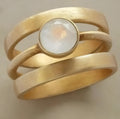 Gold geometric hollow ring with a small white chalcedony stone, on a plain background.