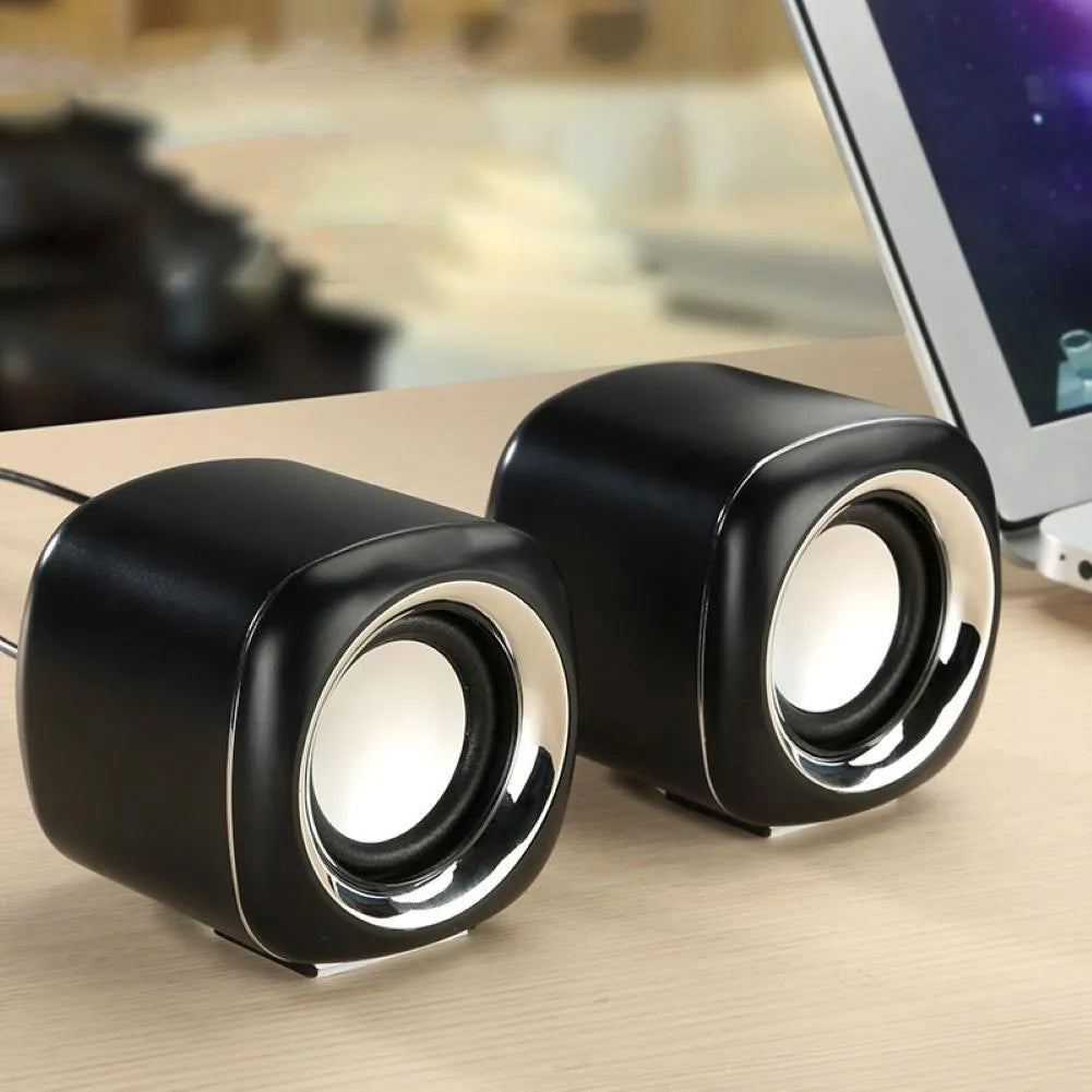Pair of compact black wired desktop computer speakers with top volume scroll wheel next to a laptop.