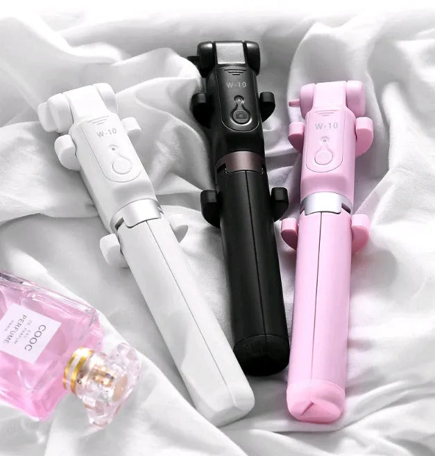 Black Bluetooth selfie stick tripod with extended rod, phone clamp, and deployed legs next to a smartphone