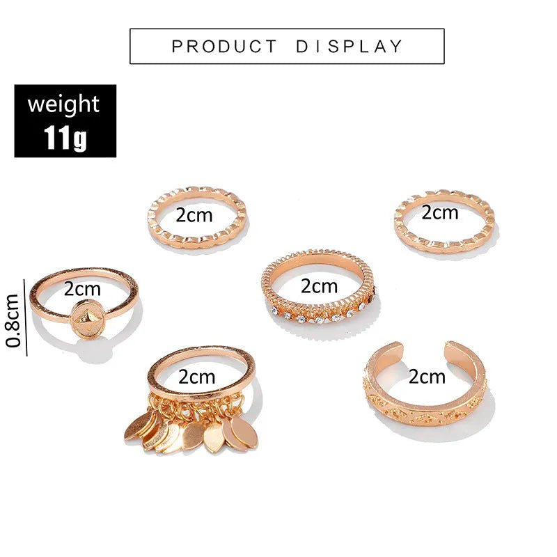 Six gold alloy rings with geometric leaf and tassel designs on a light background