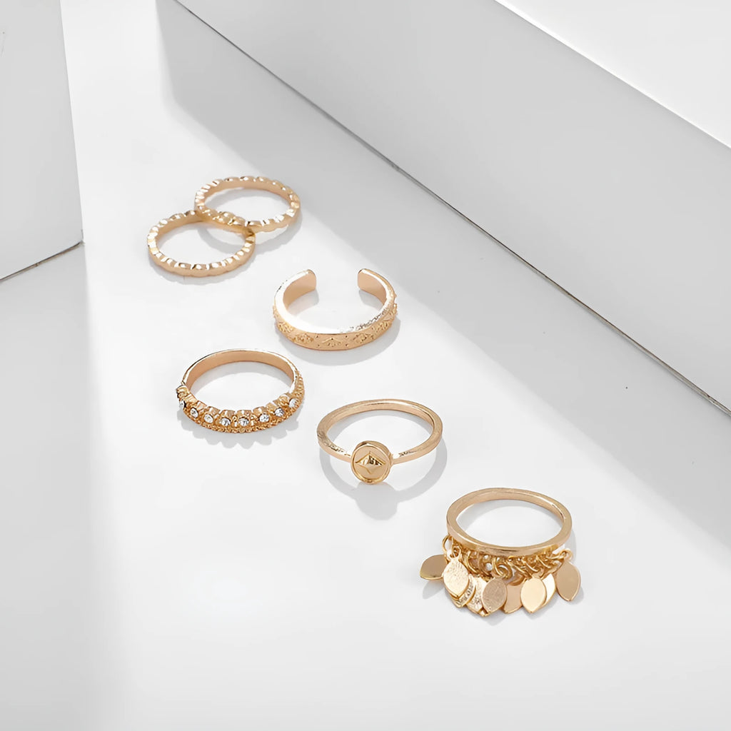 Six gold alloy rings with geometric leaf and tassel designs on a light background