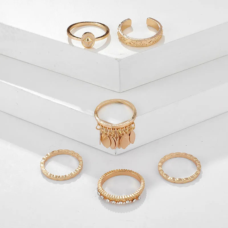 Six gold alloy rings with geometric leaf and tassel designs on a light background