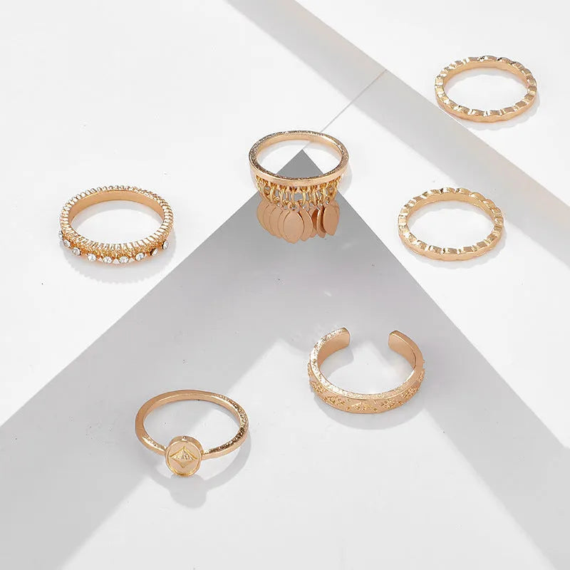 Six gold alloy rings with geometric leaf and tassel designs on a light background