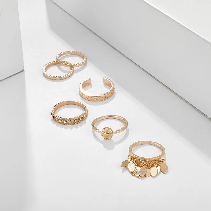 Six gold alloy rings with geometric leaf and tassel designs on a light background