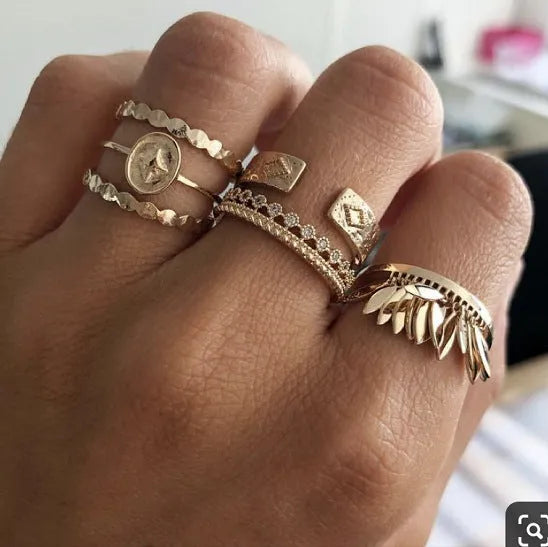 Six gold alloy rings with geometric leaf and tassel designs on a light background