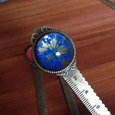 Handmade dried flower bookmark with lace flowers, daffodils, and clover, measuring 12cm long, on a book.