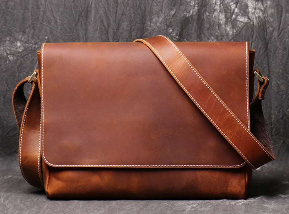 Vintage brown cowhide leather messenger bag with a shoulder strap, shown open to reveal internal ID, phone, and zipper pockets.