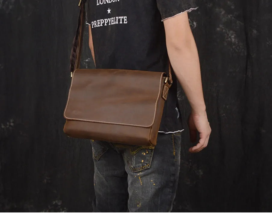 Vintage brown cowhide leather messenger bag with a shoulder strap, shown open to reveal internal ID, phone, and zipper pockets.