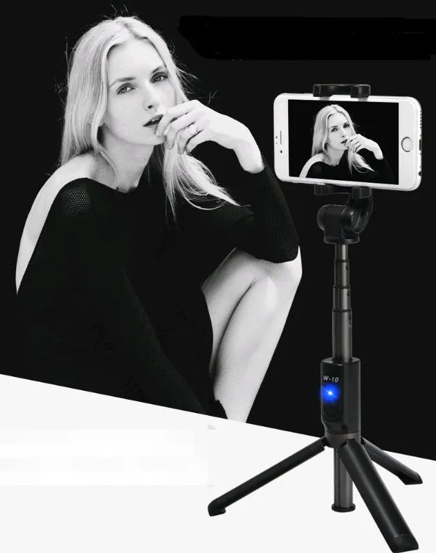 Black Bluetooth selfie stick tripod with extended rod, phone clamp, and deployed legs next to a smartphone