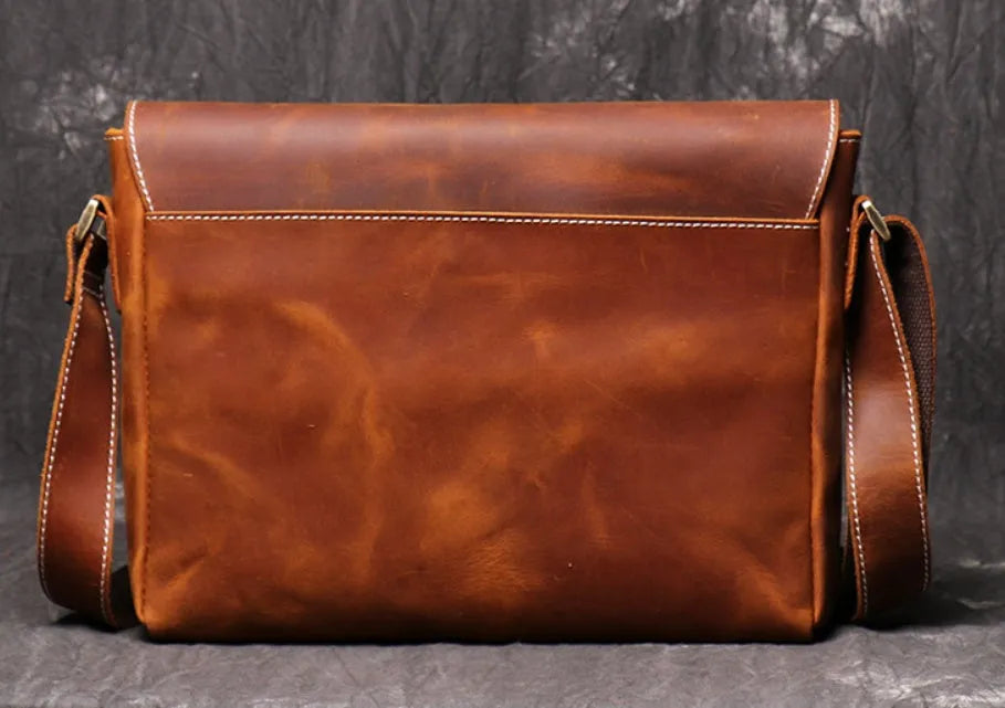 Vintage brown cowhide leather messenger bag with a shoulder strap, shown open to reveal internal ID, phone, and zipper pockets.