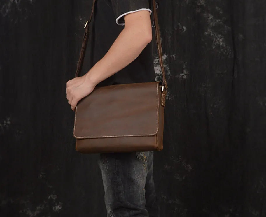 Vintage brown cowhide leather messenger bag with a shoulder strap, shown open to reveal internal ID, phone, and zipper pockets.