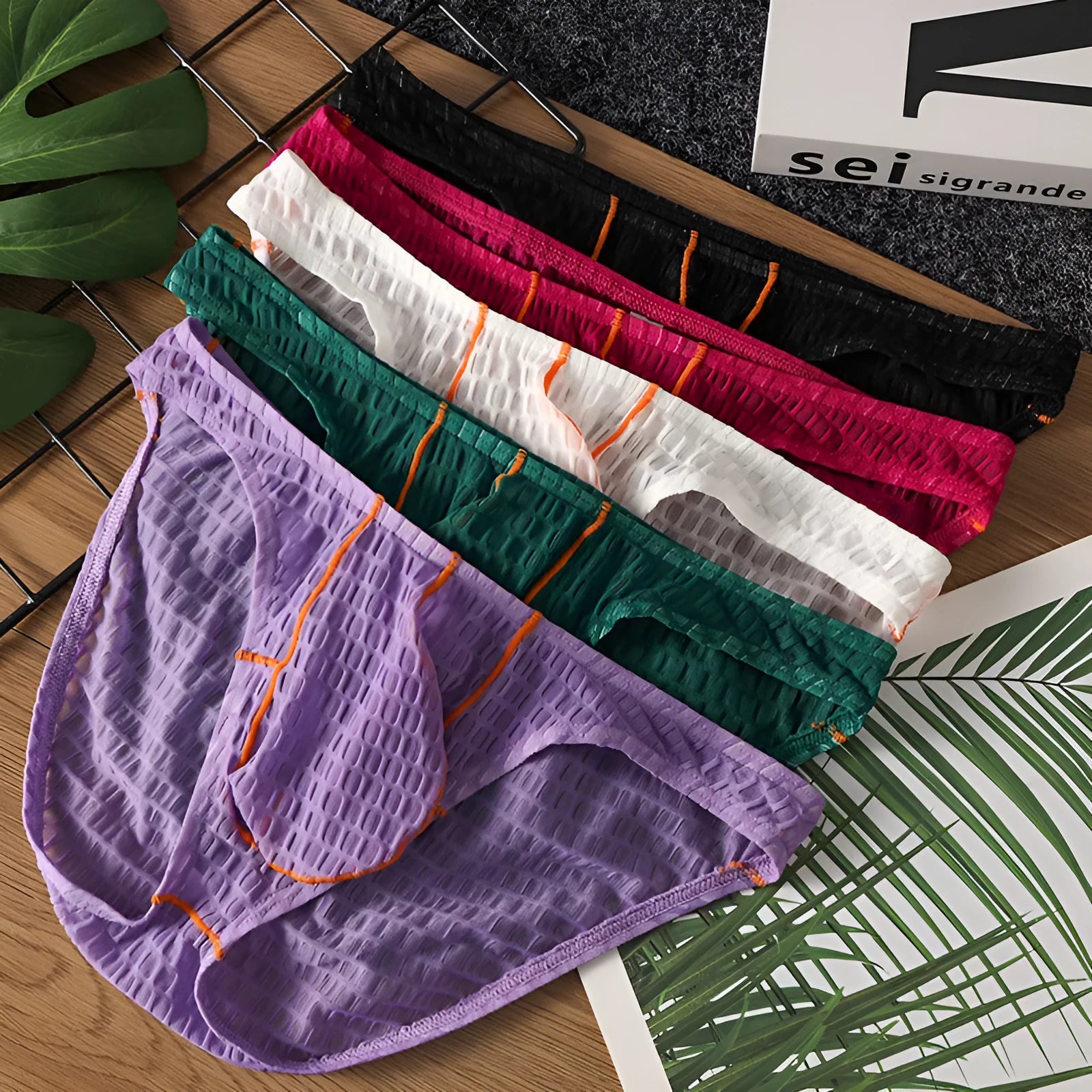 Men's low-waist lace briefs in white, black, green, red, and purple colours laid flat.
