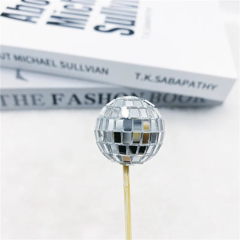 Glass disco ball cake decoration with wooden stick on a cake, showing reflective surface.