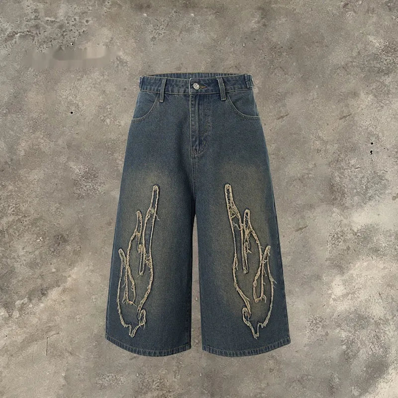 Men's black denim shorts with flame embroidery patches on the legs, showing a cropped, straight-leg cut.