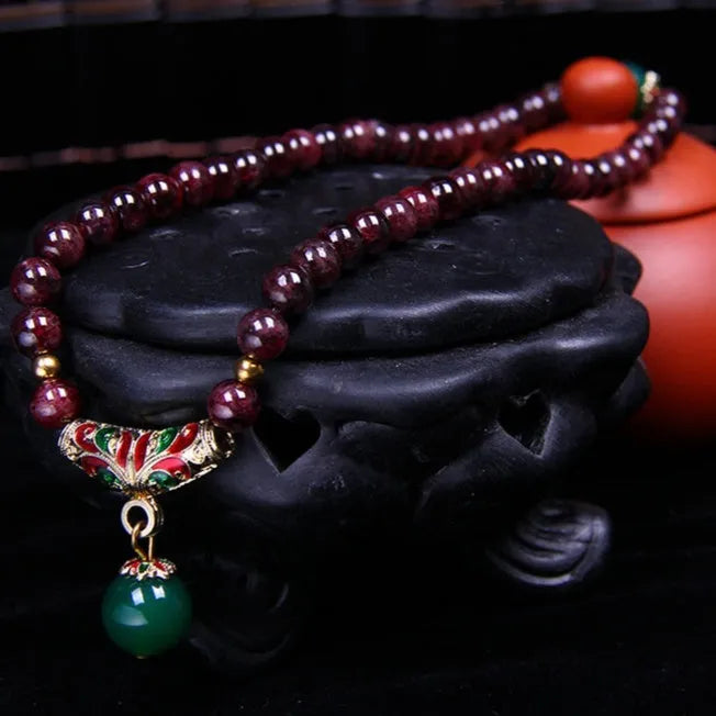 Close-up of a deep red natural garnet bracelet with 7mm beads, a golden toad charm, and a double ring clasp.