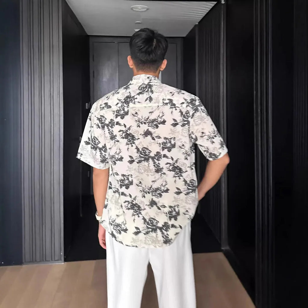 Man's loose fit black short sleeve shirt with floral pattern, worn open in cardigan style.