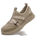 Men's grey safety work shoes with a woven upper and thick rubber sole on a work site background.