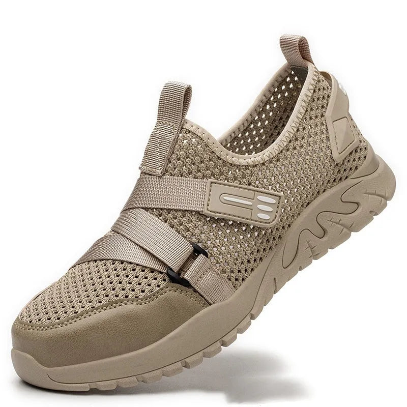 Men's grey safety work shoes with a woven upper and thick rubber sole on a work site background.