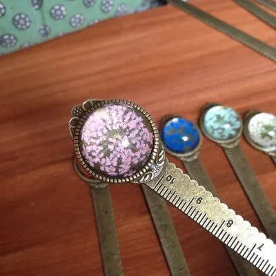 Handmade dried flower bookmark with lace flowers, daffodils, and clover, measuring 12cm long, on a book.