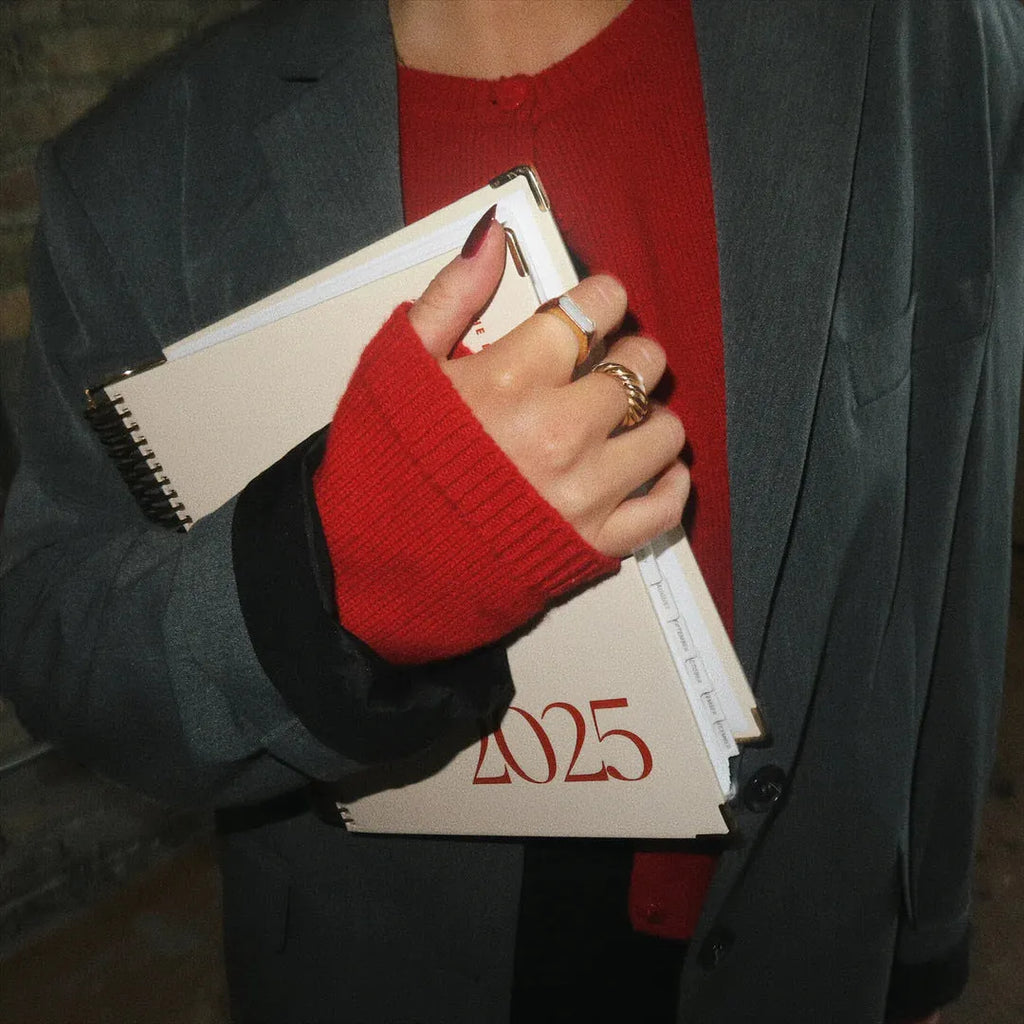 Cherry red coil notebook open on a desk, showing spiral binding and paper pages for scheduling.