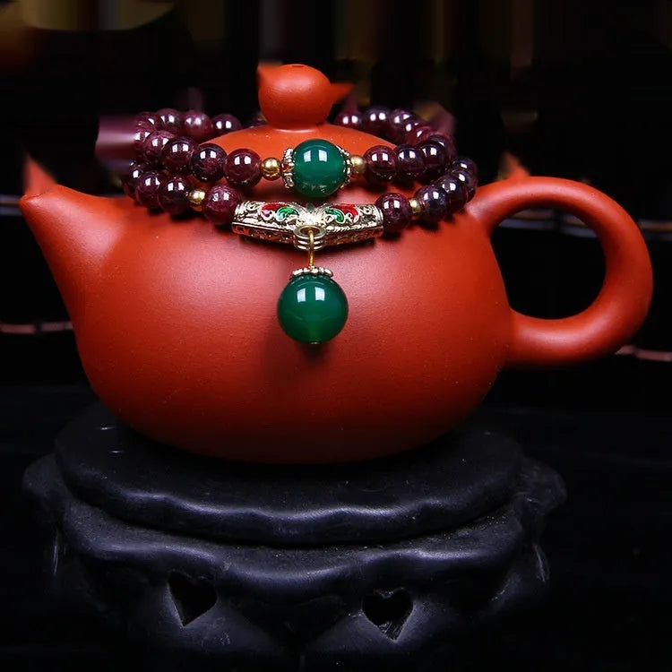 Close-up of a deep red natural garnet bracelet with 7mm beads, a golden toad charm, and a double ring clasp.