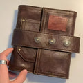 Brown PU cover A7 notebook with metal buckle closure showing loose-leaf binding and raw wood pulp pages