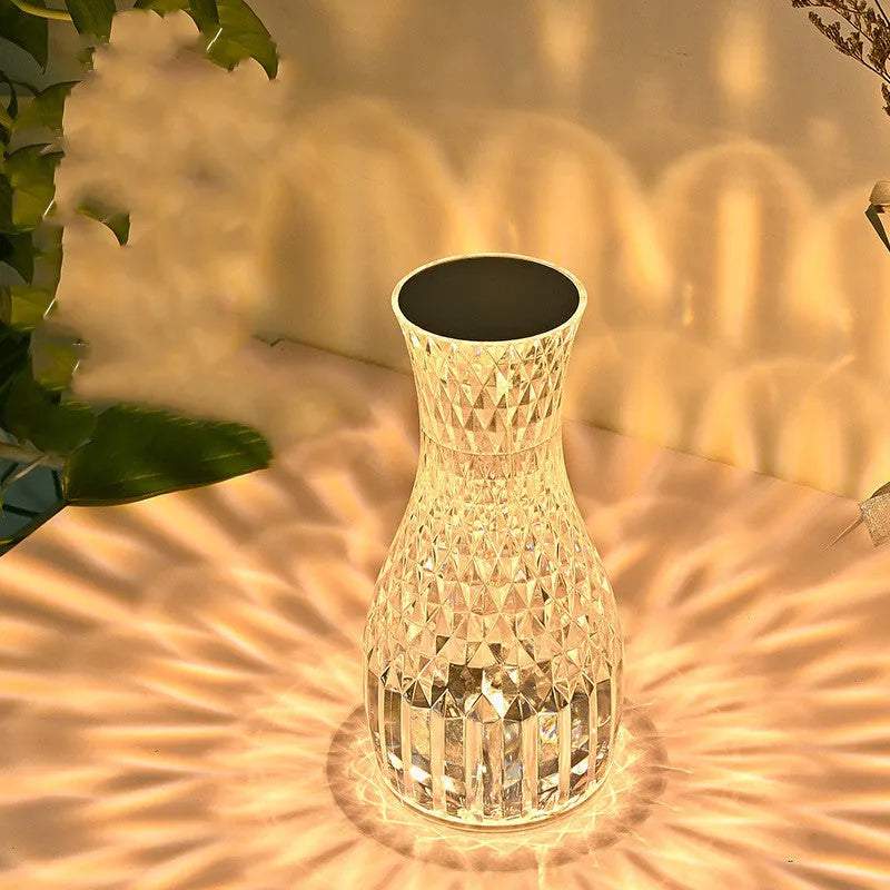 Clear plastic vase-shaped crystal bedside lamp with LED lights on a wooden table.
