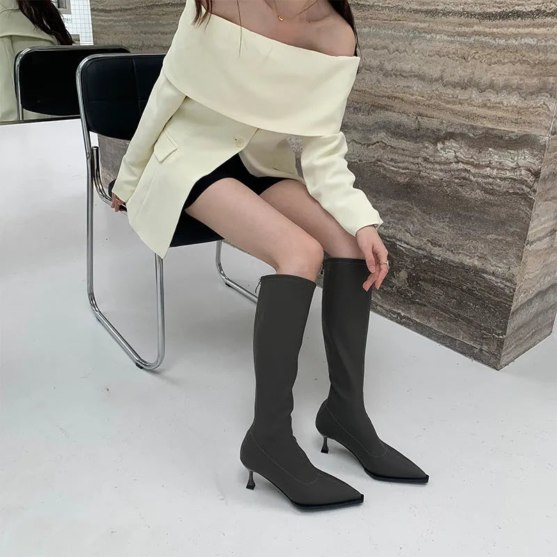 Black pointed toe women's below-the-knee boots with stiletto heel and back zipper fastening.