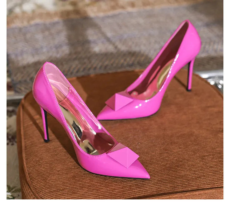 Pink women's pointed toe stiletto high heels with patent leather upper, rivet details, and a buckle.