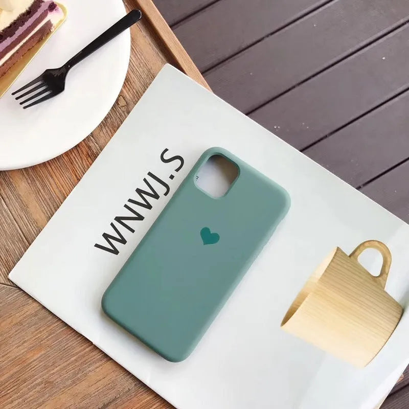 Solid colour silicone phone case for iPhone, shown in dark green, on a wooden surface.