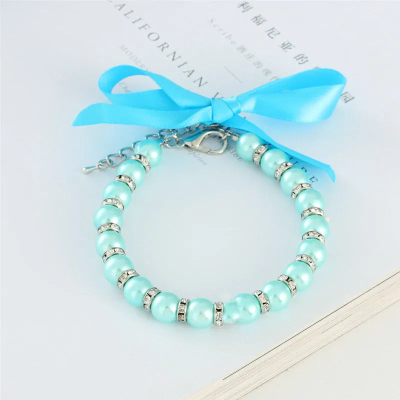 Small dog wearing blue pearl and rhinestone necklace with ribbon bow