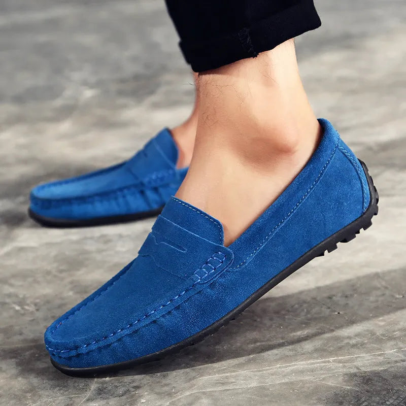 Men's suede slip-on loafers in black on a flat rubber sole, showing round toe and sewing detail.