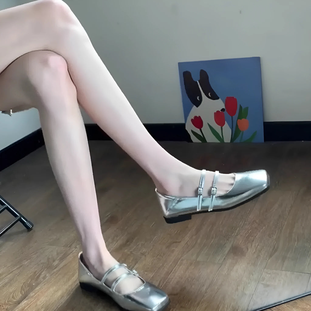 Women's silver leather Mary Jane flats with a cross buckle strap and flat sole.