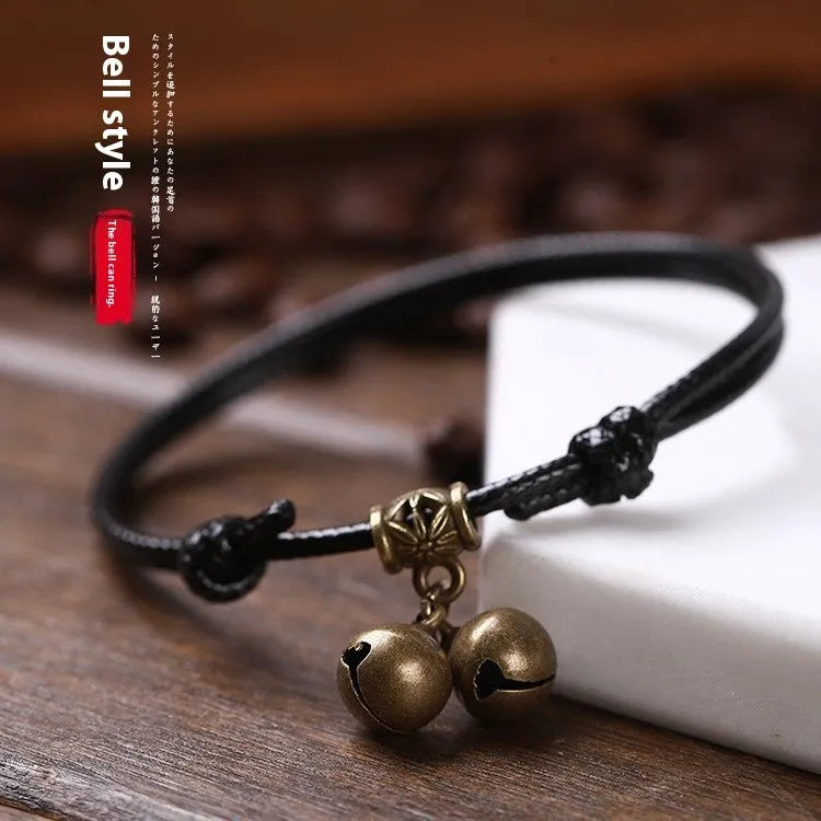 Black nylon rope dog collar with an attached brass bell lying on a wooden surface.