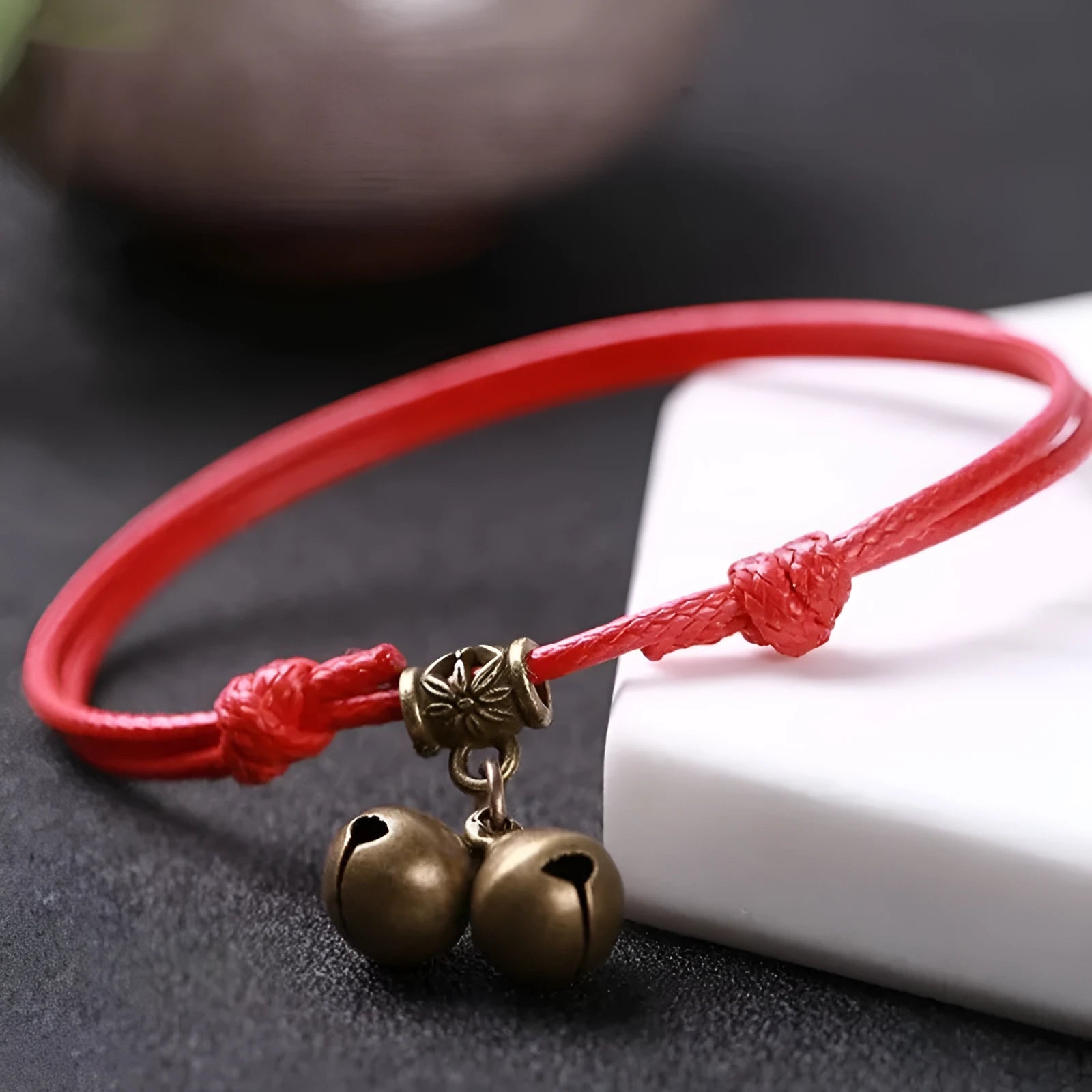 Black nylon rope dog collar with an attached brass bell lying on a wooden surface.