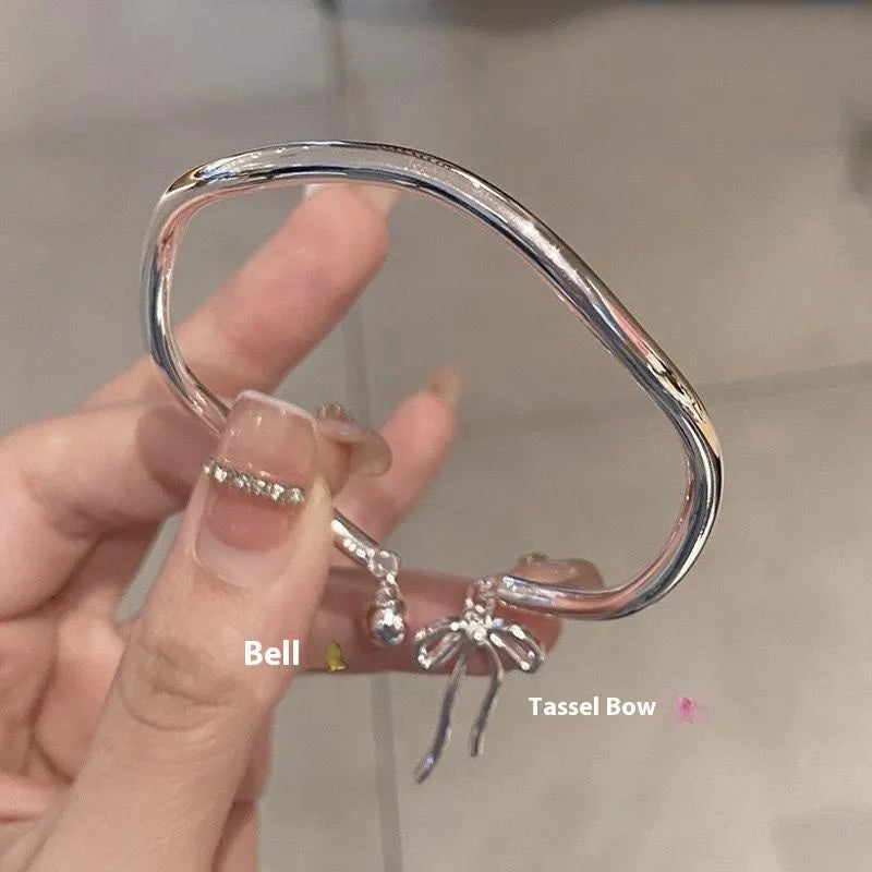 Silver adjustable bracelet with a bow charm and an opening bell charm on a model's wrist.