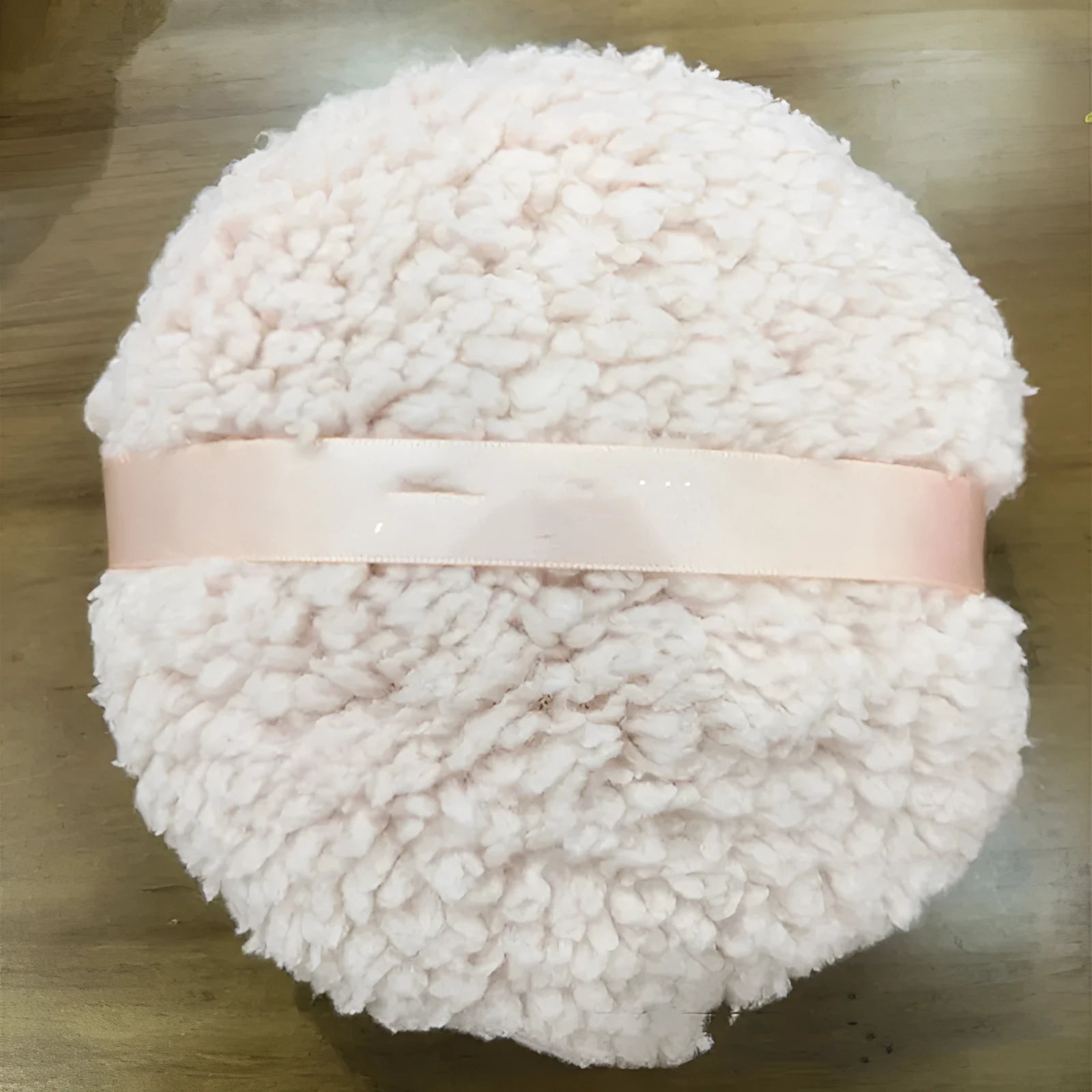Large oval white plush powder puff for makeup on a plain background.