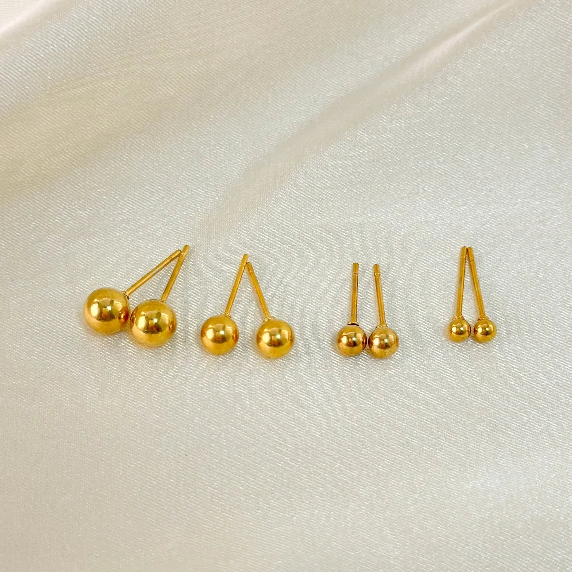 Stainless steel ball stud earrings in gold and silver finishes on a grey background.