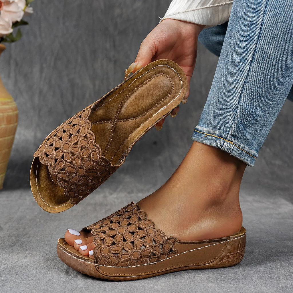 Women's black beach slippers with flower cutout design on the PVC upper and a rubber wedge sole.