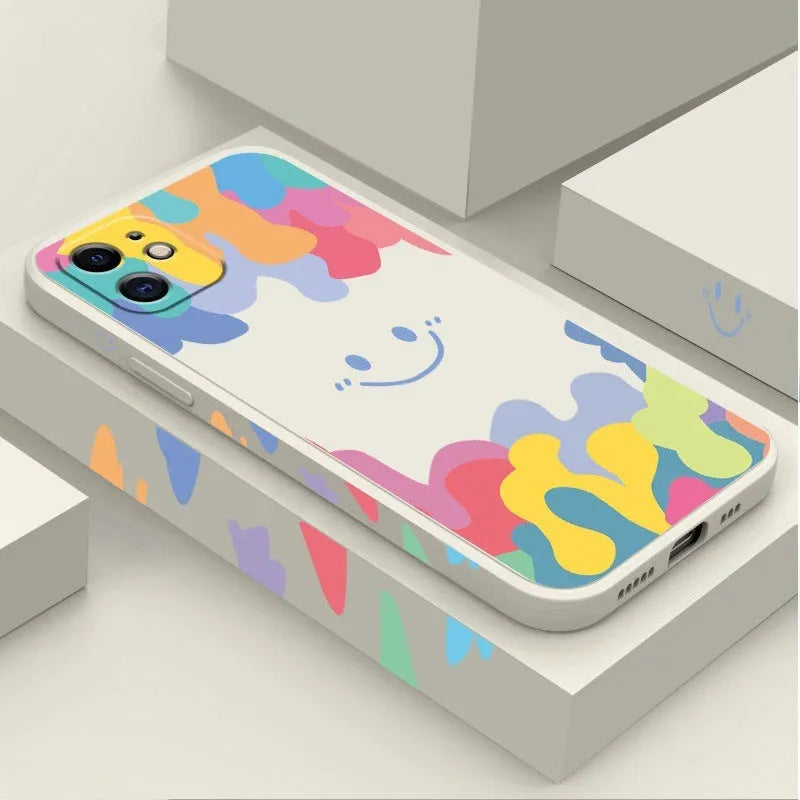 White and black silicone iPhone cases featuring a large rainbow smiley face design, shown with attached lanyards.